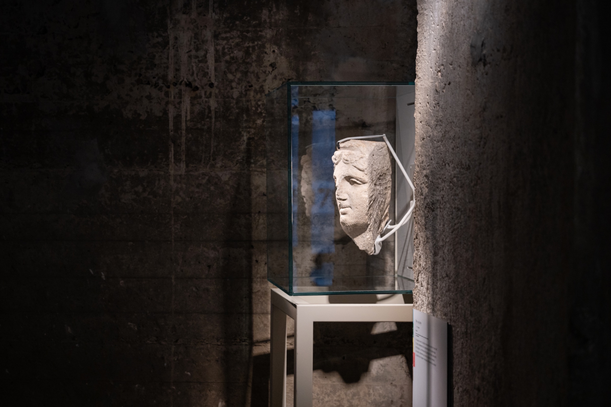 Buste antique dans une vitrine, éclairé par une lumière douce, fond industriel.