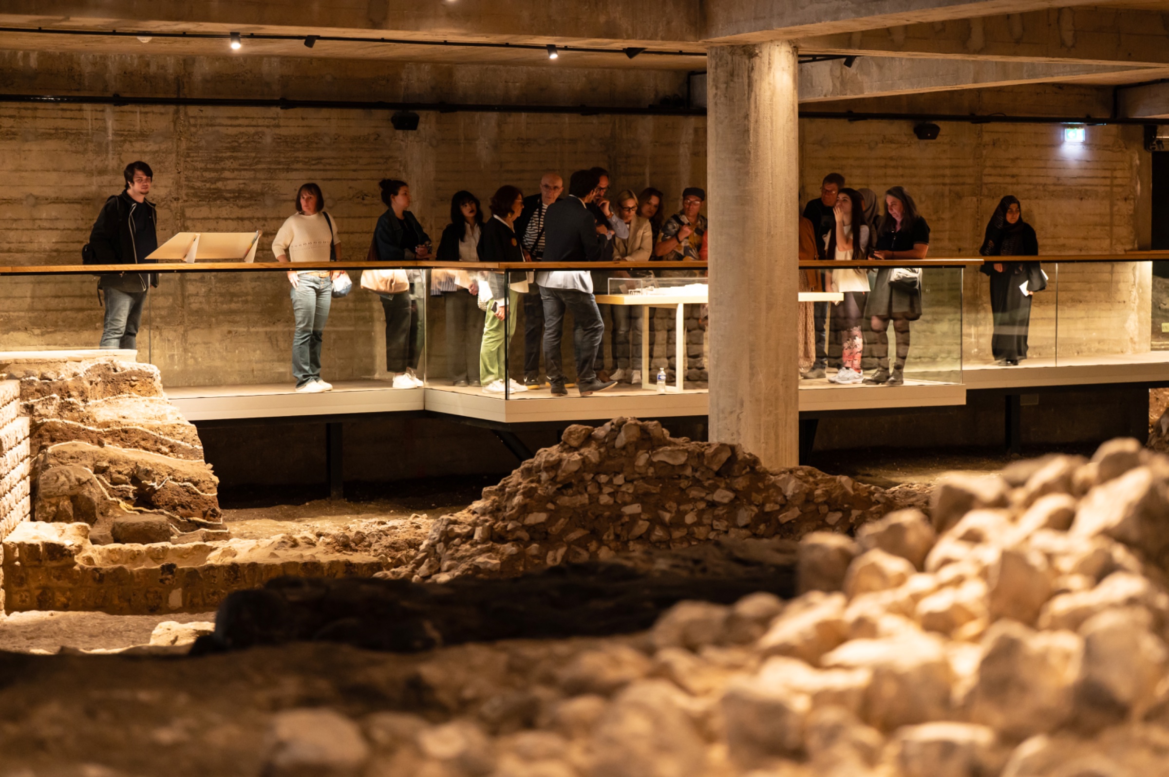 Des visiteurs observent des fouilles archéologiques dans un espace muséal moderne.